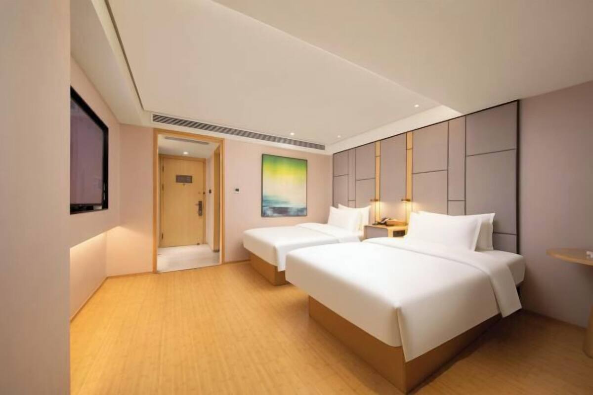 A hotel room with two beds, a painting, a nightstand, and a wooden floor.