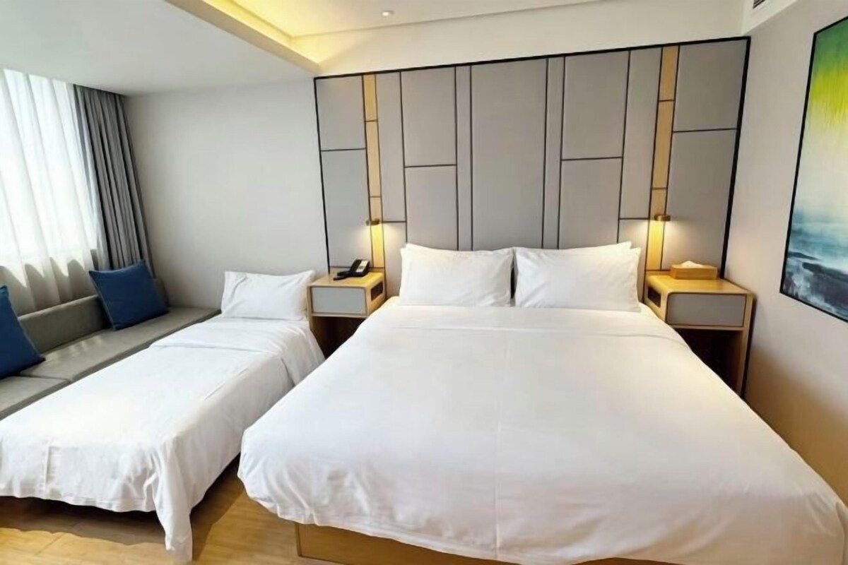 A hotel room with two beds, a sofa, and a large window with curtains.