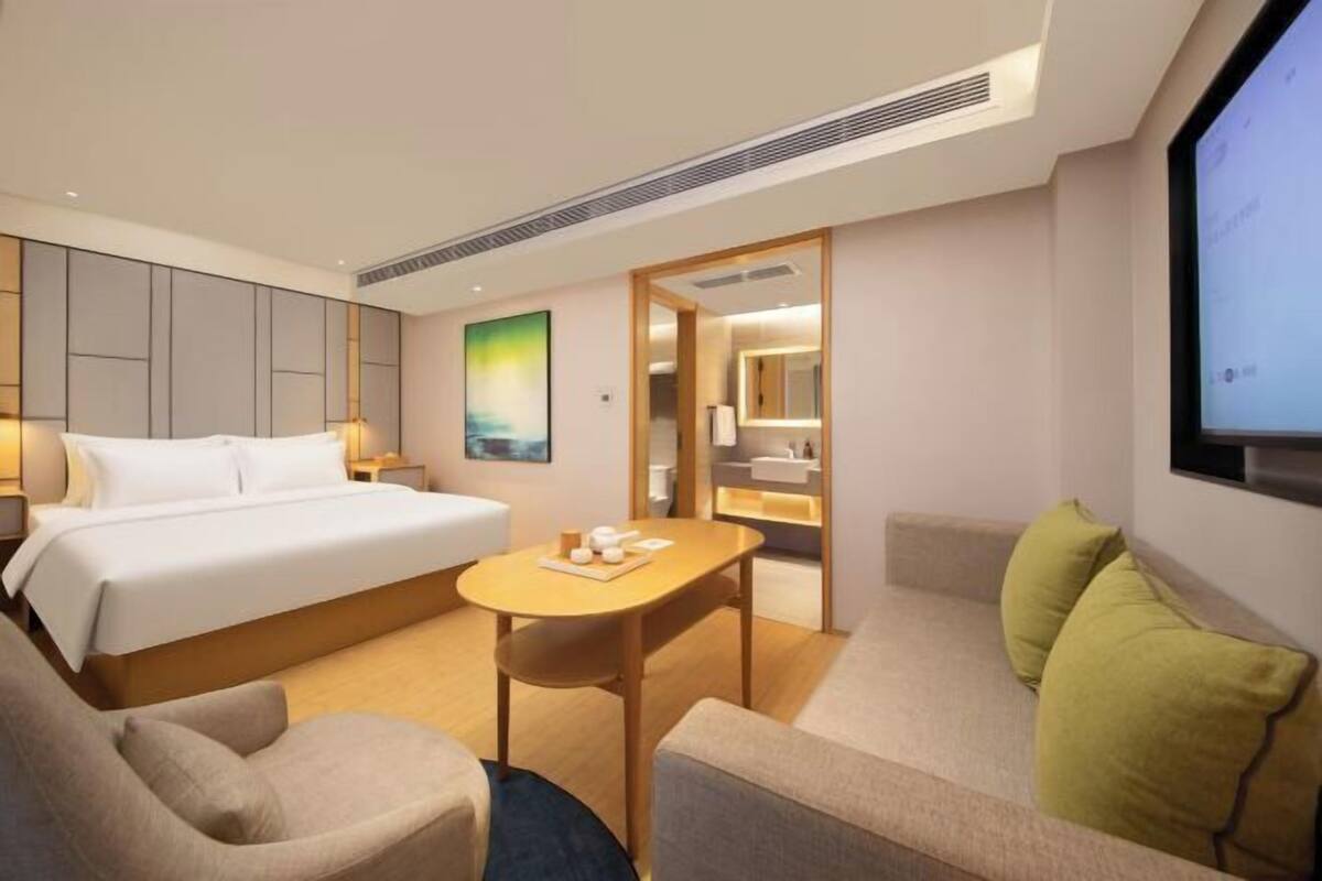 A hotel room with a bed, a desk, a chair, a sofa, and a TV screen.