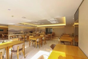 A modern dining area with multiple tables and chairs, a kitchen area, and a large window providing natural light. - JI Hotel (Wuhan Hankou Railway Station Tangjiadun) (Wuhan)