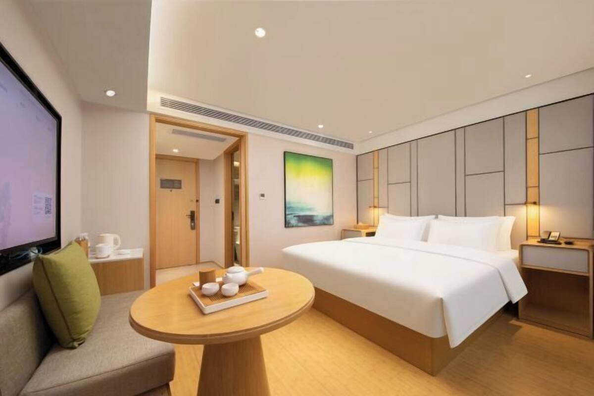 A hotel room with a bed, a round table with tea set, a TV, and a painting on the wall.