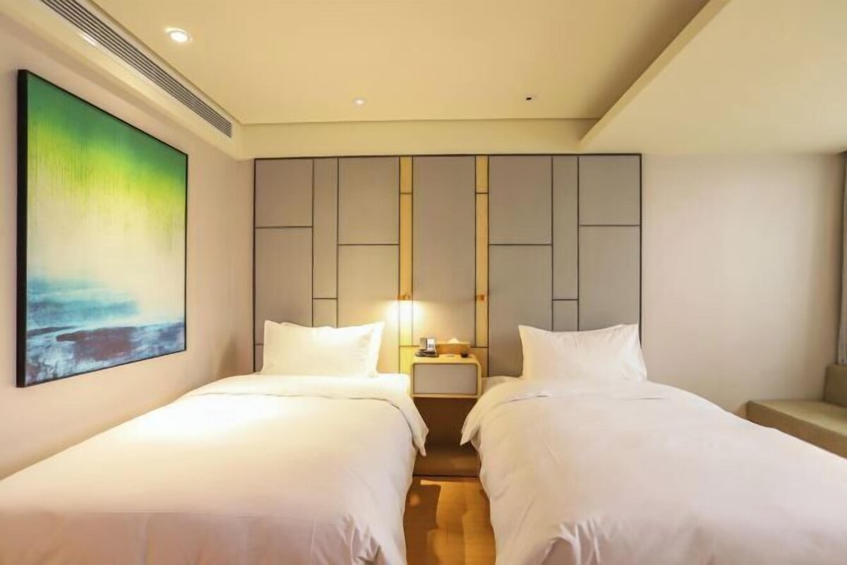 A hotel room with two beds, a large abstract painting on the wall, and a modern wardrobe.