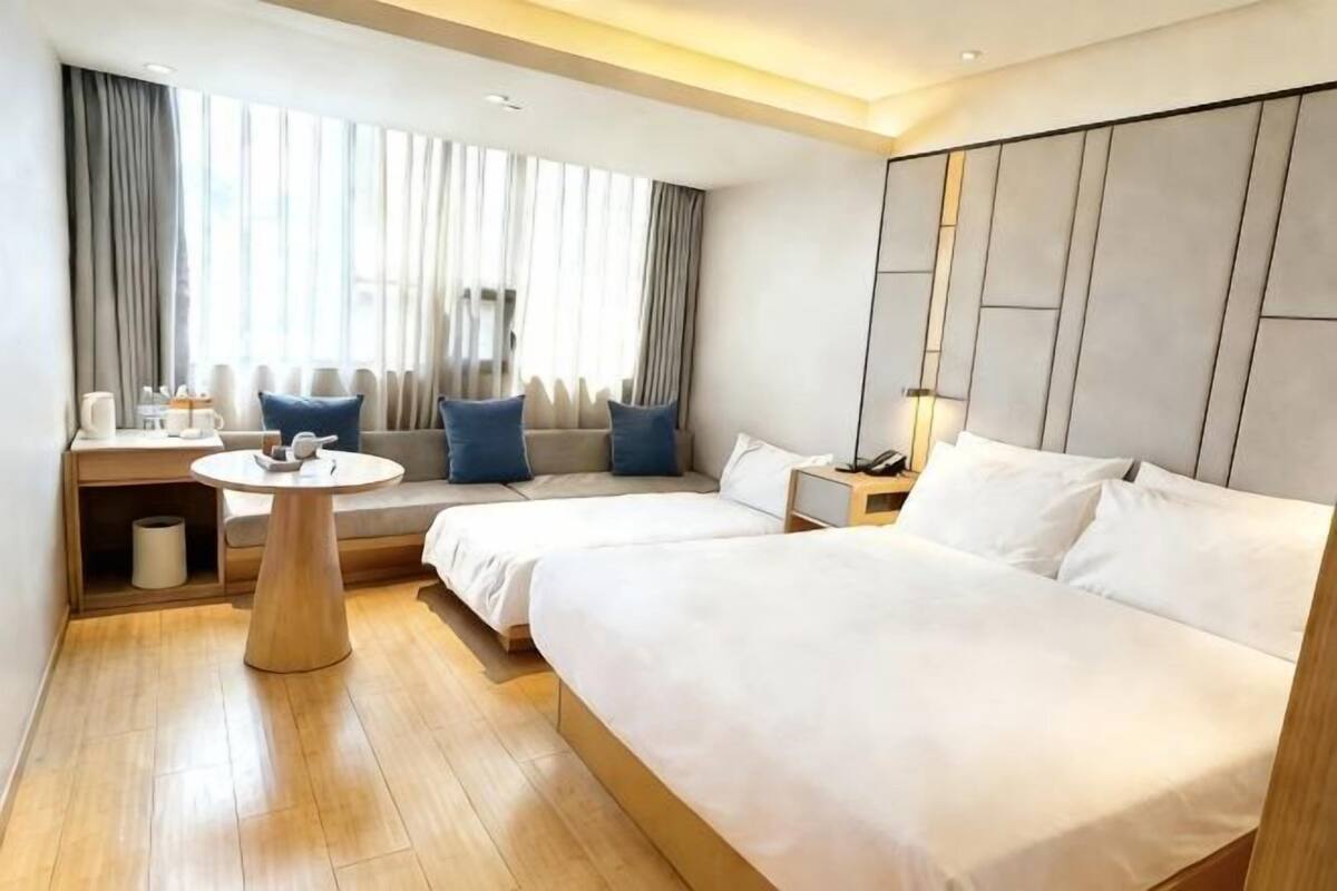 A hotel room with a bed, bedside table, lamp, and a window with curtains.