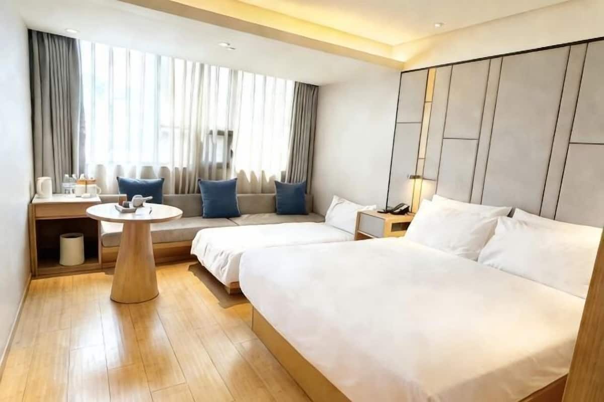 A hotel room with a bed, bedside table, lamp, and a window with curtains.