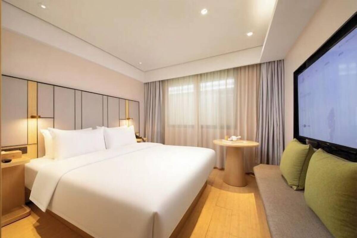 A modern hotel room with a large bed, a round table, and a television.
