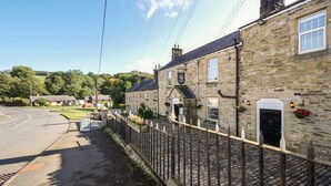 A stone building with a pub sign, a cobblestone street, and a grassy area in the background. - The Greenhead Hotel (Brampton)