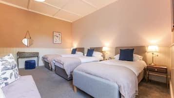 Une chambre d’hôtel avec trois lits simples, un petit bureau, une chaise et une table de chevet avec une lampe.