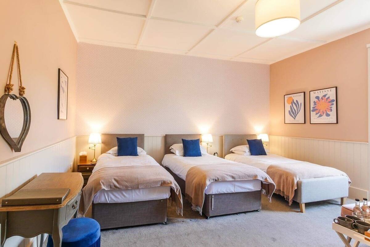 A hotel room with two beds, a desk, a chair, and a small table with bottles and glasses.