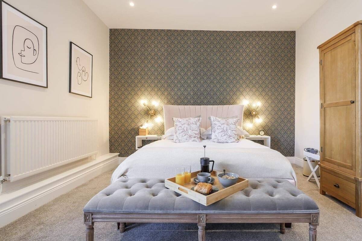 A bedroom with a large bed, a wooden wardrobe, a bedside table with a lamp, and a tray with breakfast items.