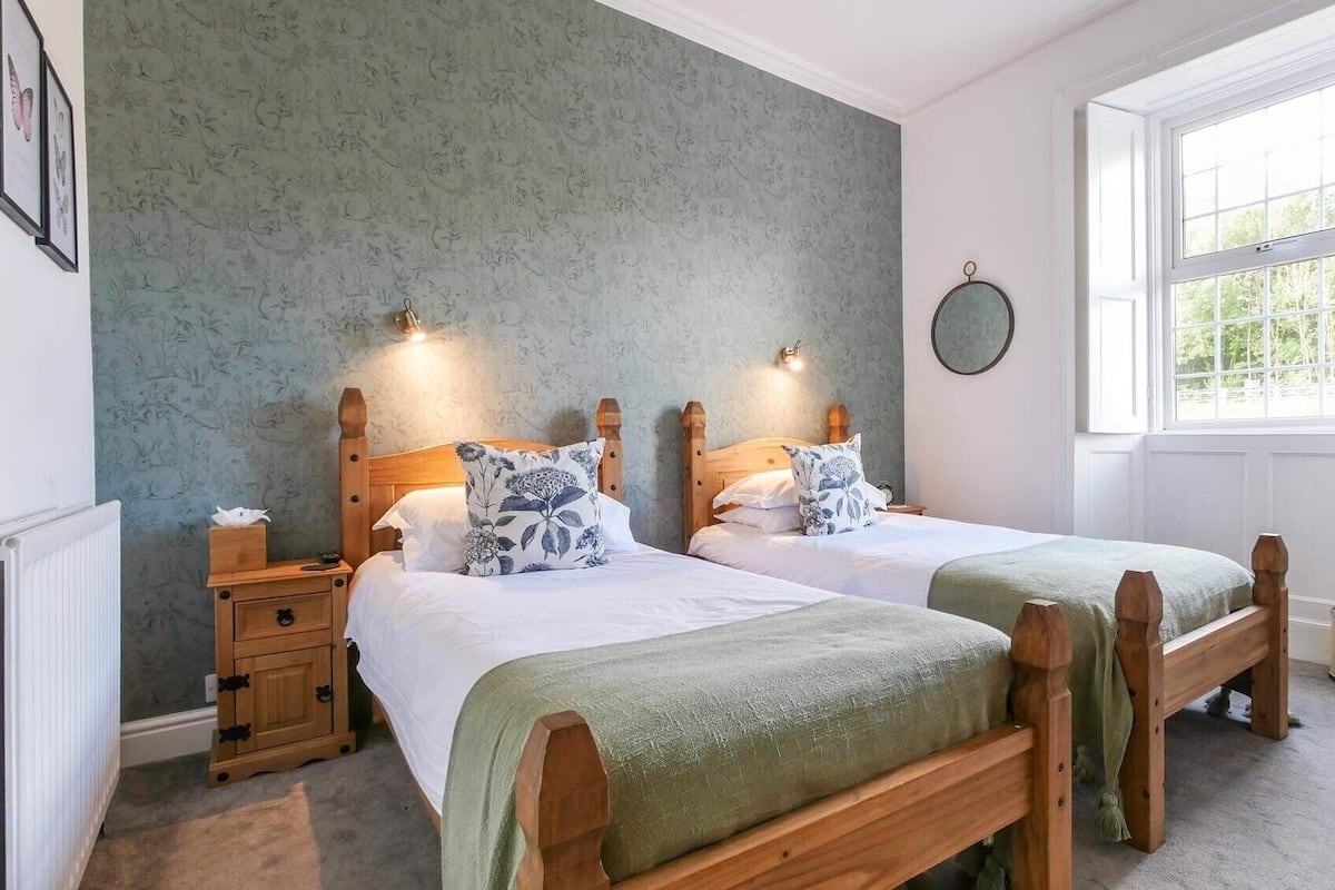 A bedroom with two wooden beds, a radiator, a window, and a wall clock.