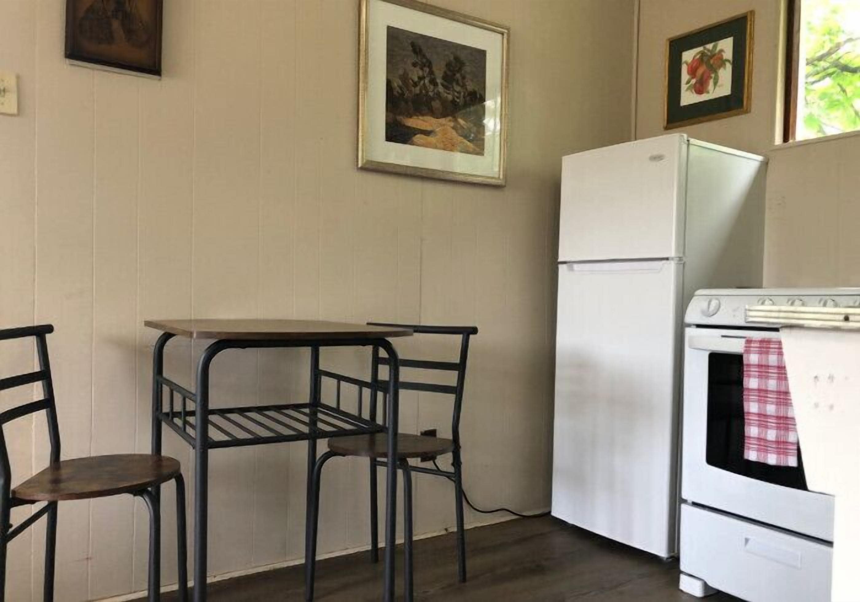 A compact kitchen with a white refrigerator, a stove, and a small dining table with two chairs.