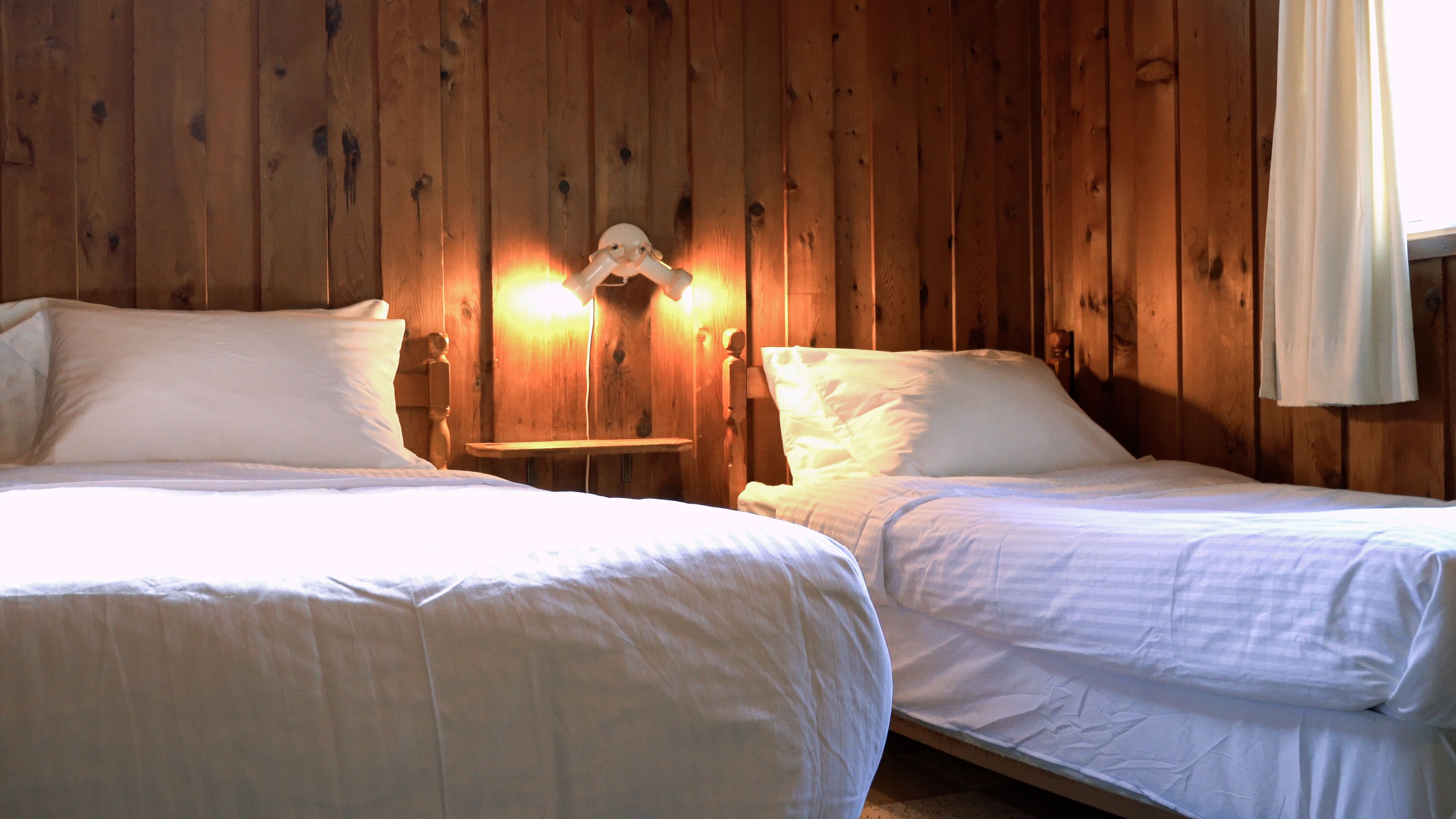 Une chambre avec deux lits, des murs en bois et une table de chevet avec une lampe.
