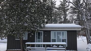 Une petite cabane avec une table de pique-nique et des bancs, le tout abrité, et entourée d’arbres couverts de neige.