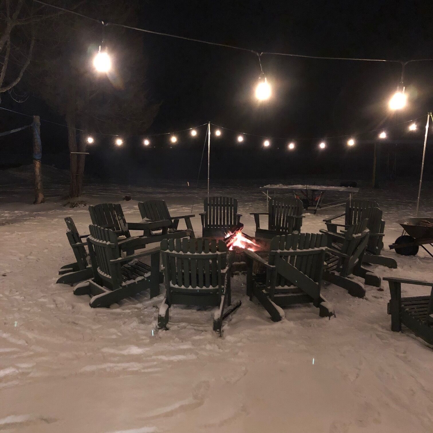 Un espace extérieur aménagé avec des chaises Adirondack disposées autour d’un foyer central, le tout entouré de neige.
