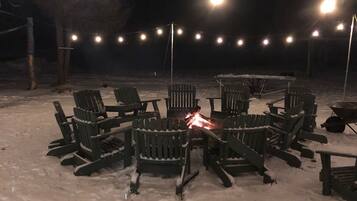 Un espacio de estar al aire libre con sillas Adirondack dispuestas alrededor de un hogar central, rodeado de nieve.