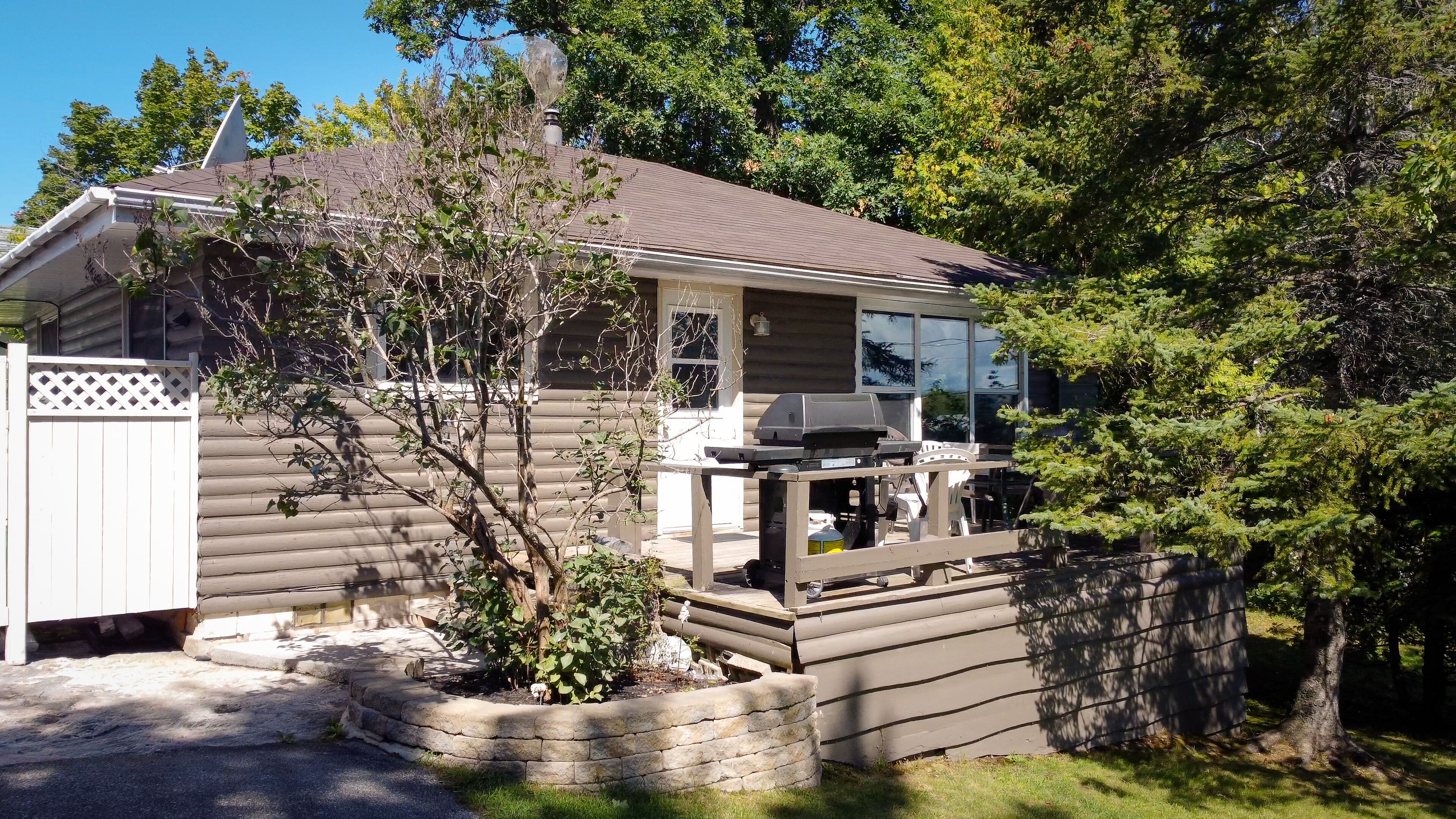 A log cabin with a deck, a chimney, and a stone retaining wall.