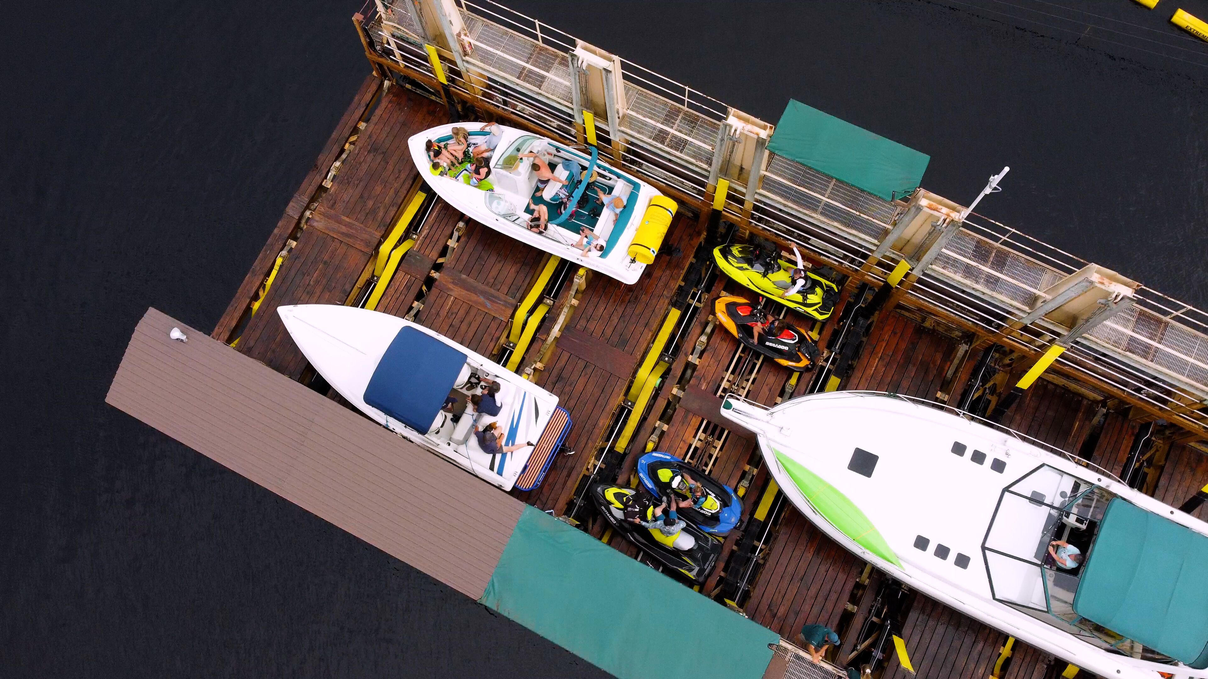 A dock with various boats and watercraft, including a white speedboat, a jet ski, and a motorboat.