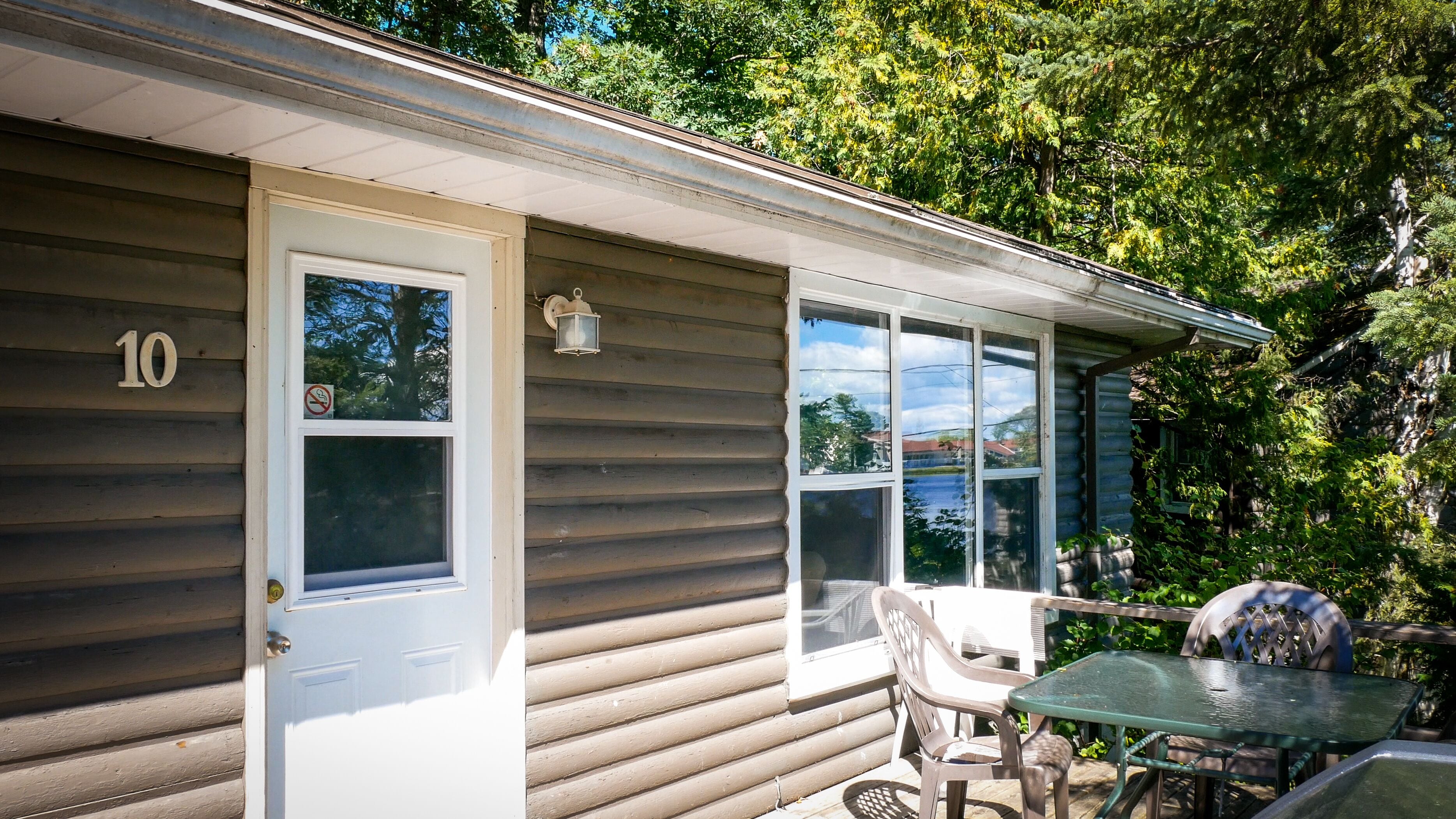A small cabin with a number 10 sign, a door, and windows. There is a table and chairs outside.