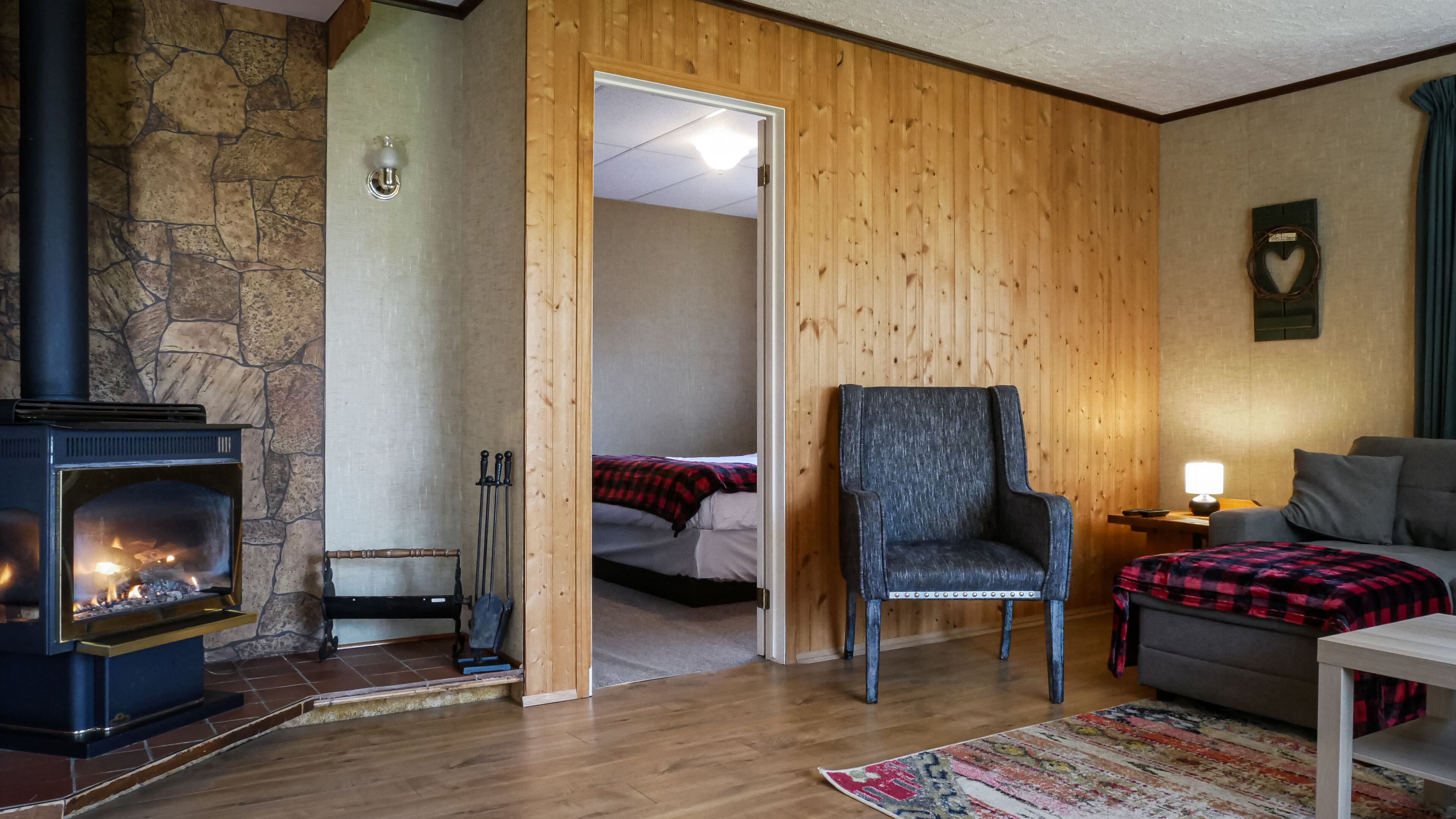 A cozy room with a stone wall, a fireplace, a wooden door, a bed, a chair, a sofa, and a rug.