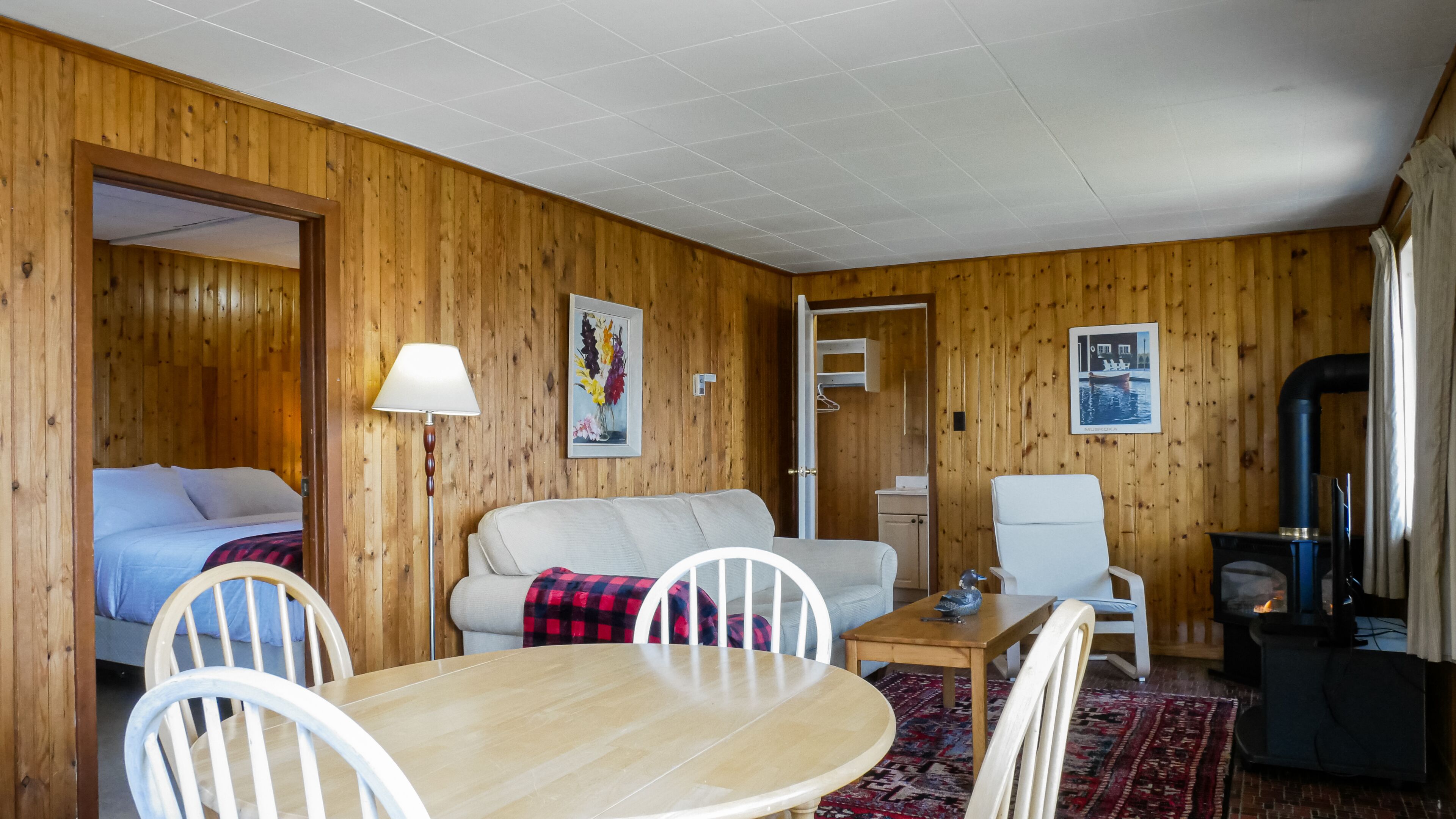 L’intérieur d’un chalet en bois comprend un lit, un canapé, une table à manger, des chaises, une lampe, une cheminée et un tableau.