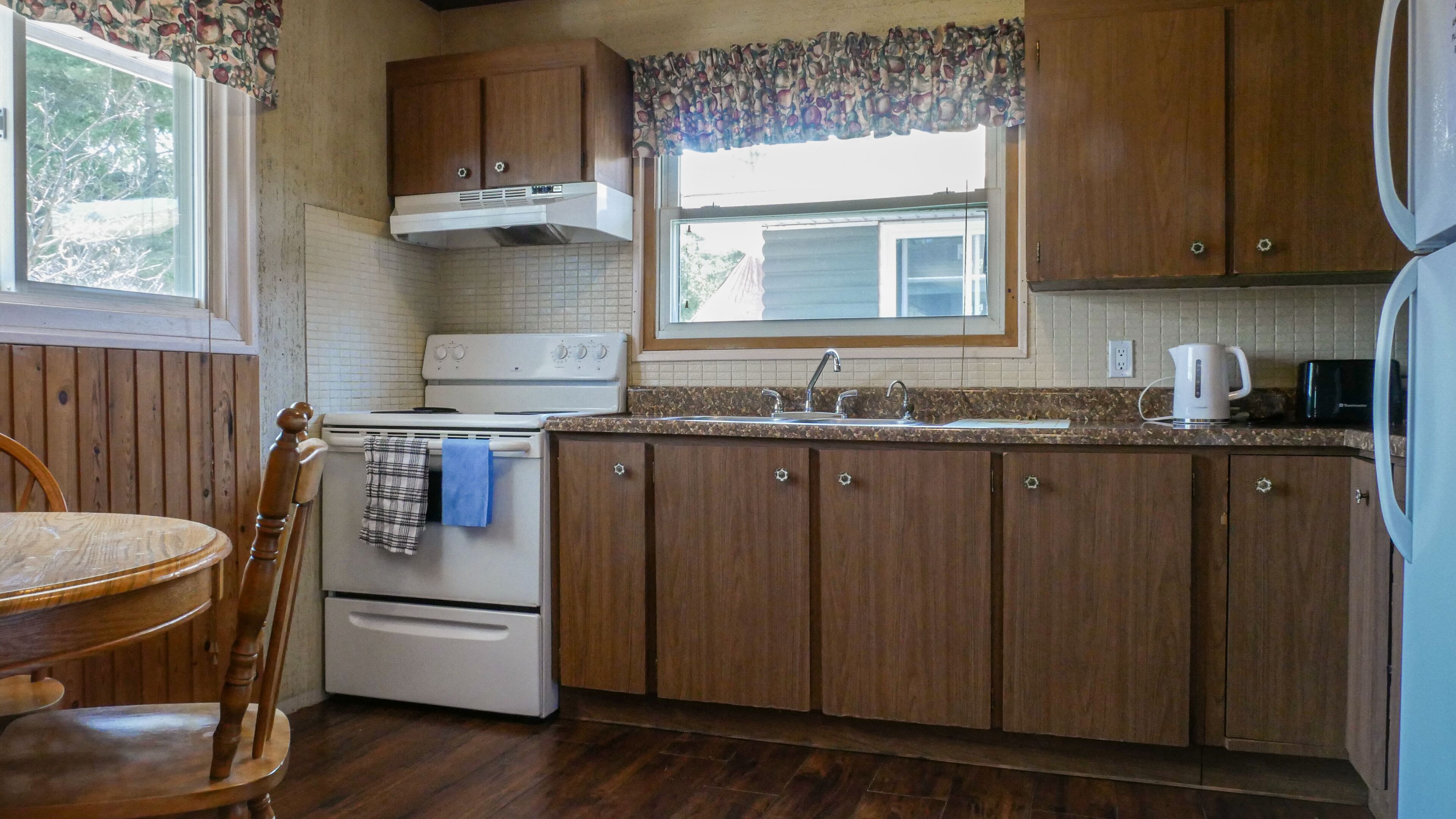 A compact kitchen with wooden cabinets, a stove, a sink, and a window with a view of the outside.
