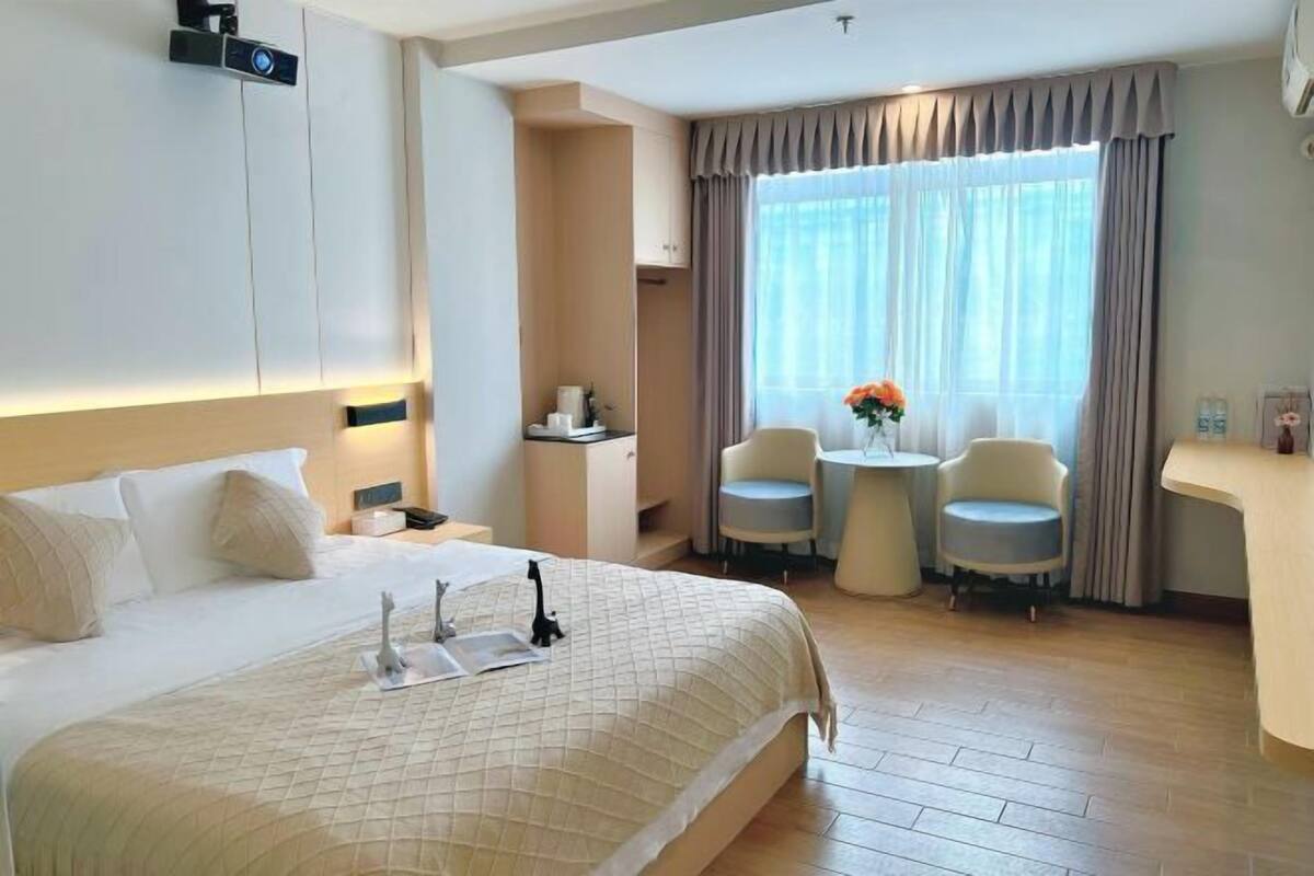 A hotel room with a large bed, bedside tables, a desk, two chairs, and a window with curtains.