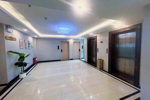 Un hall de hotel con suelo de baldosas, dos puertas, una planta en maceta y un ascensor.
