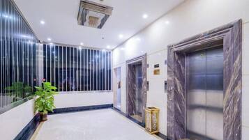 A hotel lobby with marble flooring, a potted plant, and two elevators with marble doors.