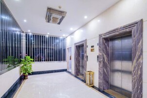 A hotel lobby with marble flooring, a potted plant, and two elevators with marble doors.