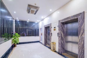 A hotel lobby with marble flooring, a potted plant, and two elevators with marble doors. - Zhaoqing Jinyuan Hotel (Zhaoqing)