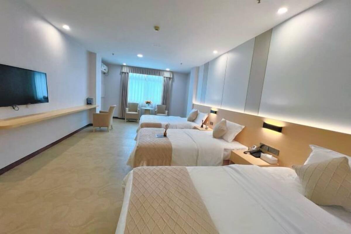 A hotel room with three beds, a TV, a desk, and a chair.