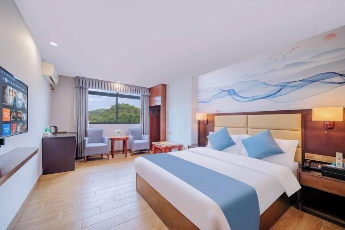 A hotel room with a large bed, a desk, a chair, and a view of the outdoors.