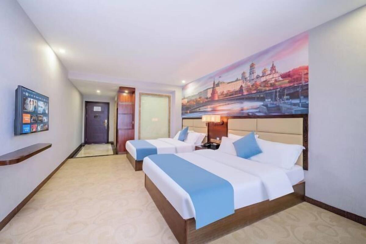 A hotel room with two beds, a large painting on the wall, a TV on the wall, and a door leading to another room.