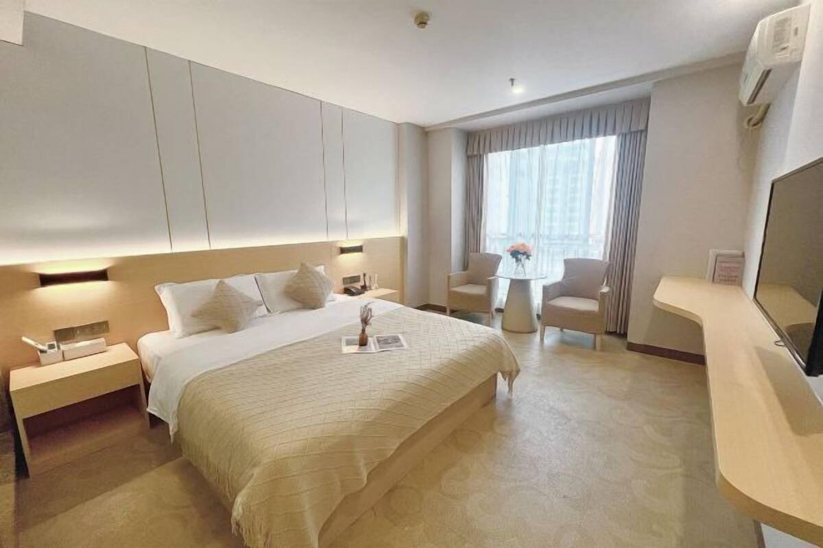 A hotel room with a bed, bedside tables, a desk, a chair, a TV, and a window with curtains.