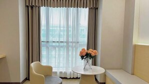 A hotel room with a large window, a round table, a sofa, and a vase with flowers. - Zhaoqing Jinyuan Hotel (Zhaoqing)