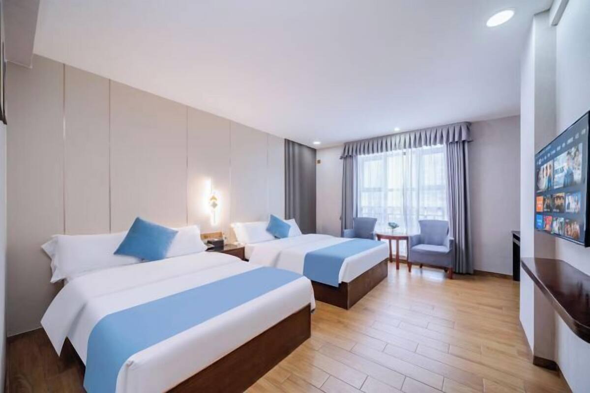 A hotel room with two beds, a small table, a chair, and a TV on the wall.