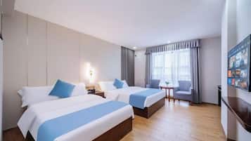Quarto de hotel com duas camas, uma mesa pequena, uma cadeira e uma televisão na parede.