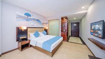 A hotel room with a bed, bedside table, lamp, artwork, TV, and a door leading to another room.