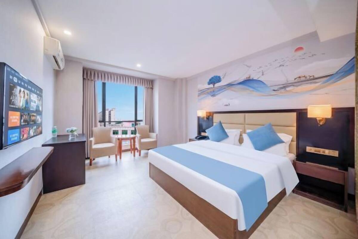 A hotel room with a large bed, a desk, a chair, a TV, and a window with curtains.