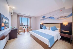 Habitación de hotel con una cama grande, un escritorio, una silla, un televisor y una ventana con cortinas.