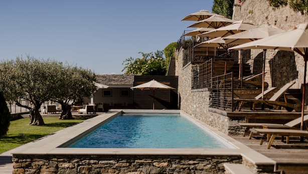 Una piscina con muros de piedra, rodeada de sillones de descanso y sombrillas.