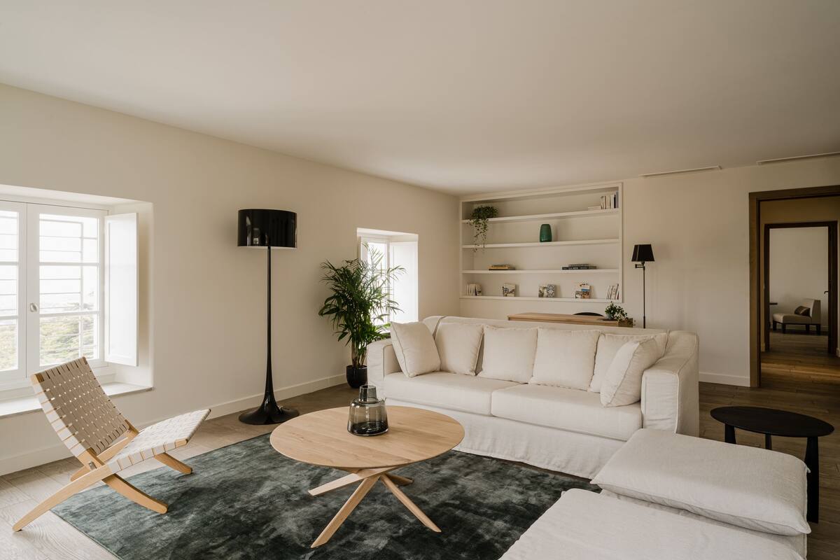 A modern living room with a white sofa, a wooden coffee table, a wicker chair, a floor lamp, and a bookshelf.