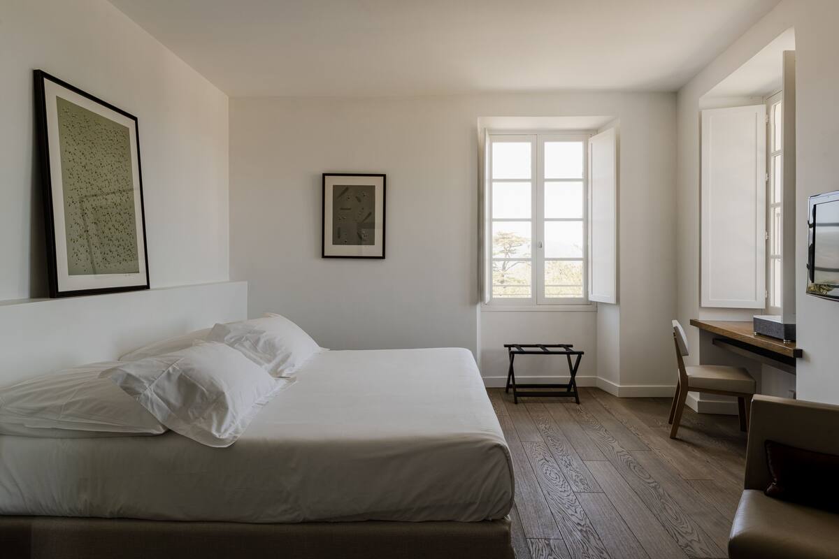 A bedroom with a bed, a desk, a chair, and a window.