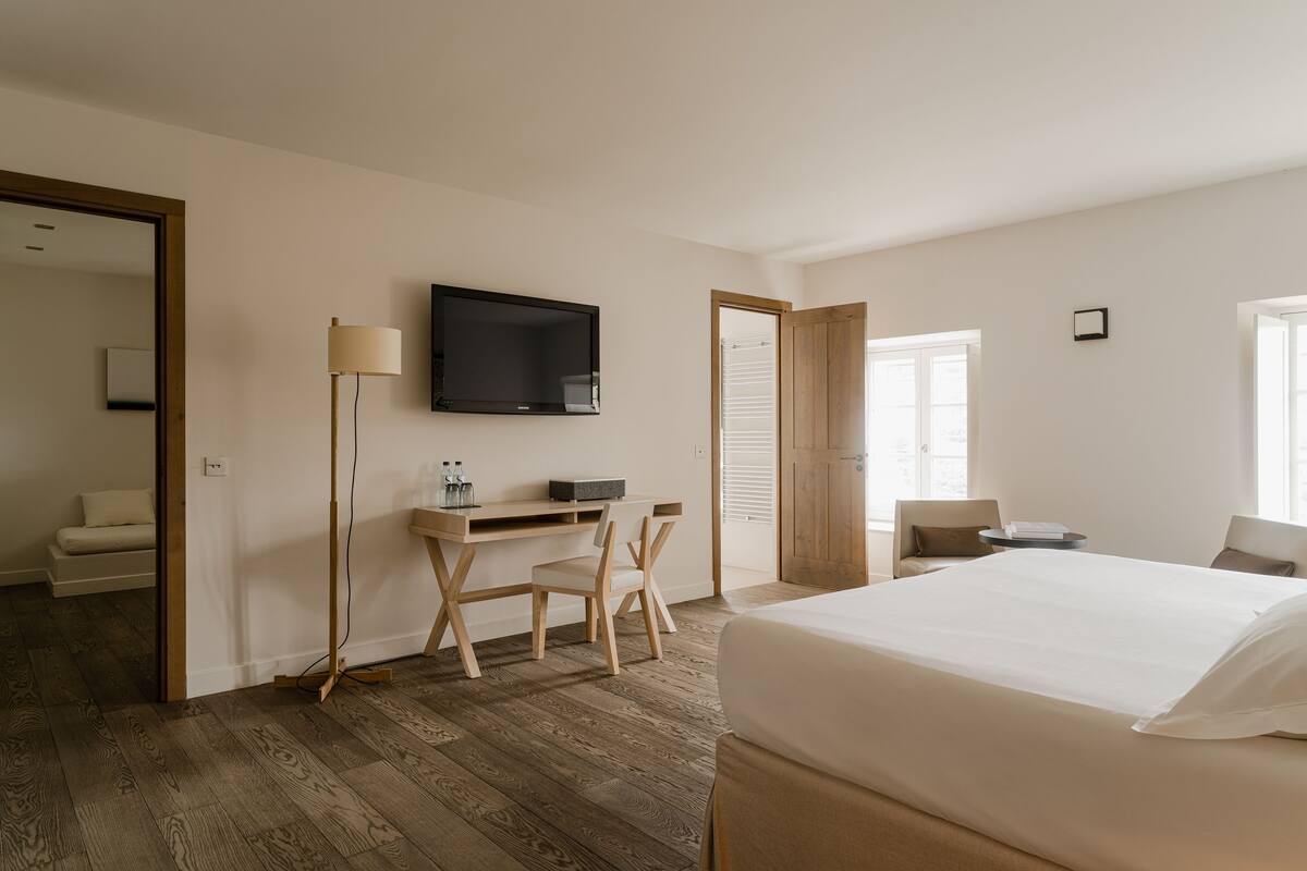 A hotel room with a bed, a desk with a chair, a TV mounted on the wall, and a window.
