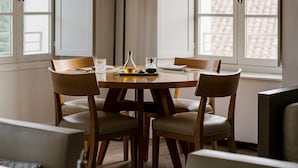 Un comedor con una mesa redonda, seis sillas, una lámpara de pie y ventanas amplias con contraventanas abiertas.