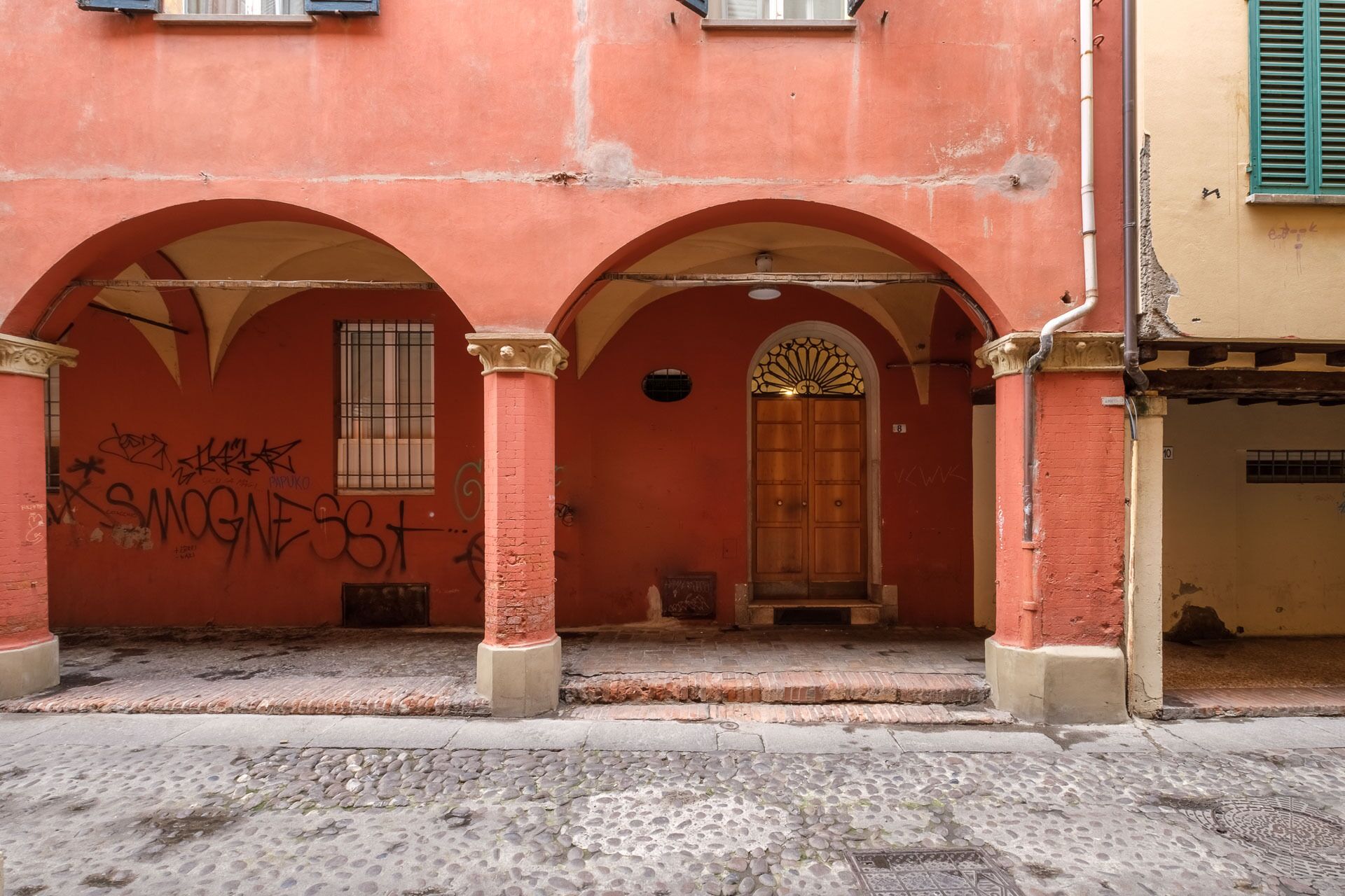 Un bâtiment à la façade rouge, doté de deux portes en arc de cercle et d’une porte en bois surmontée d’un arc décoratif.