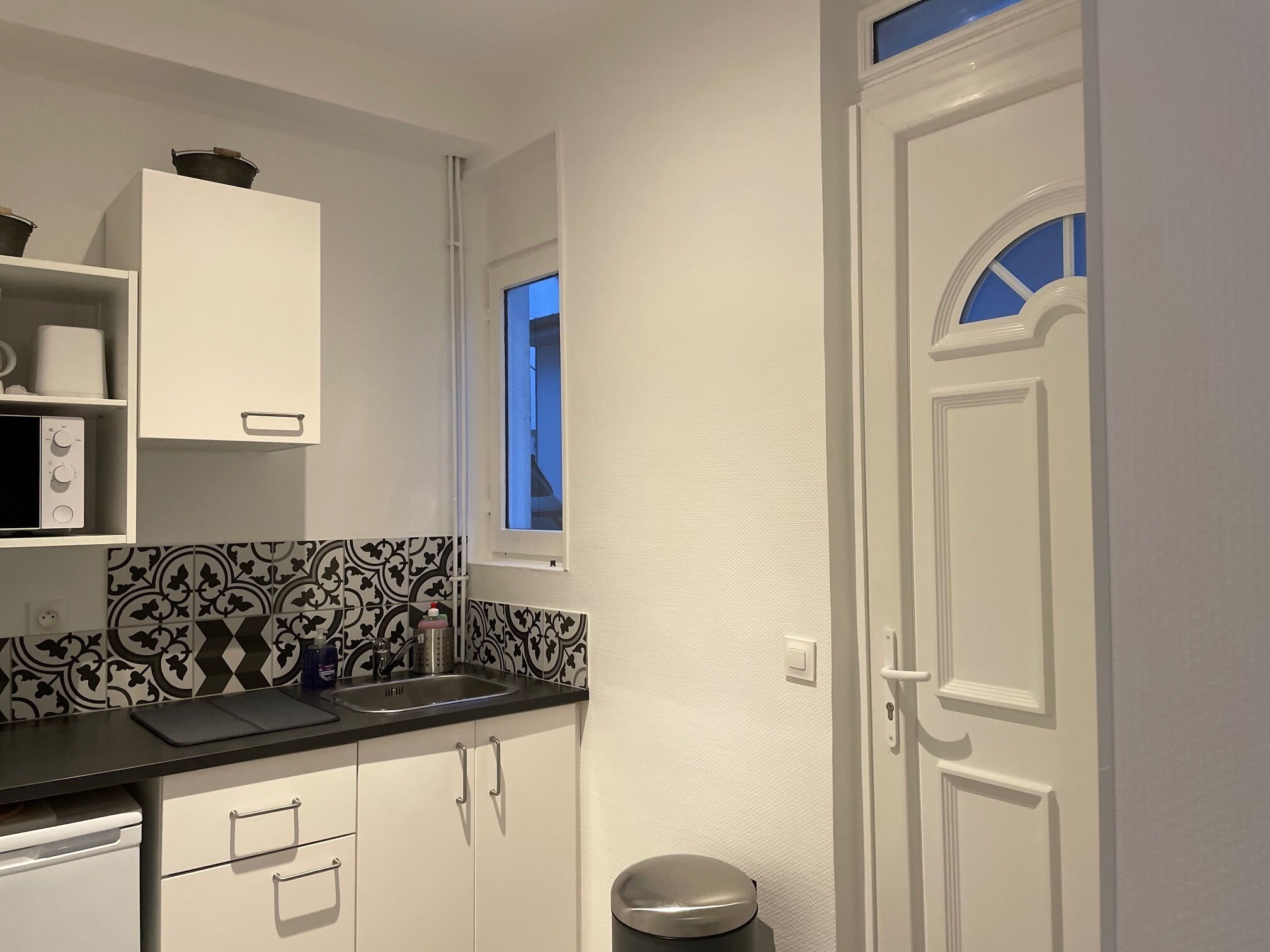 A compact kitchen with white cabinets, a black countertop, and a window above the sink.
