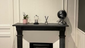 A room with a fireplace, a framed photo on the wall, and a small table with decorative items. - Le Bonnie- Ground floor studio for 2 persons (Honfleur)