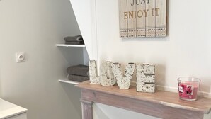 A modern bathroom with a geometric patterned floor, a white sink, a wooden vanity, a decorative wall sign, and a small shelf with a candle. - Le Bonnie- Ground floor studio for 2 persons (Honfleur)