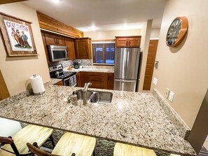 A modern kitchen with granite countertops, stainless steel appliances, wooden cabinets, and a built-in oven.